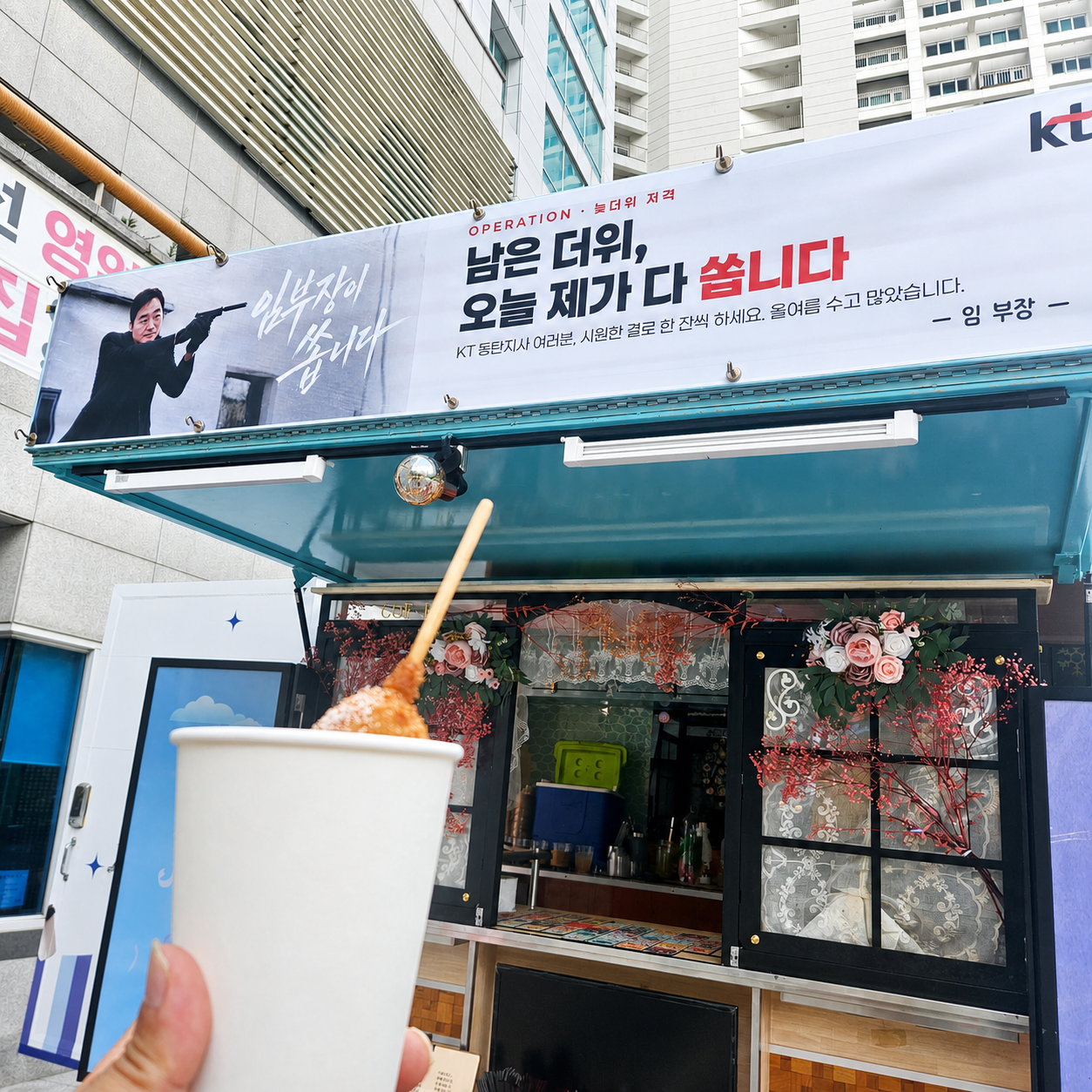 KT 동탄지사 응원 현수막과 푸드트럭 앞에서 컵 간식을 든 모습